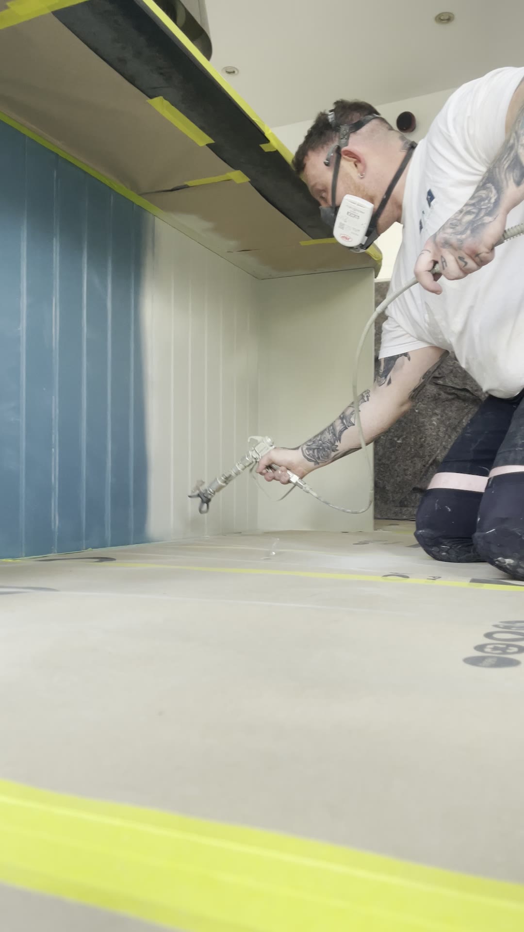 Kitchen sprayer in a respirator spraying the inside of a blue kitchen island unit with an airless spray gun