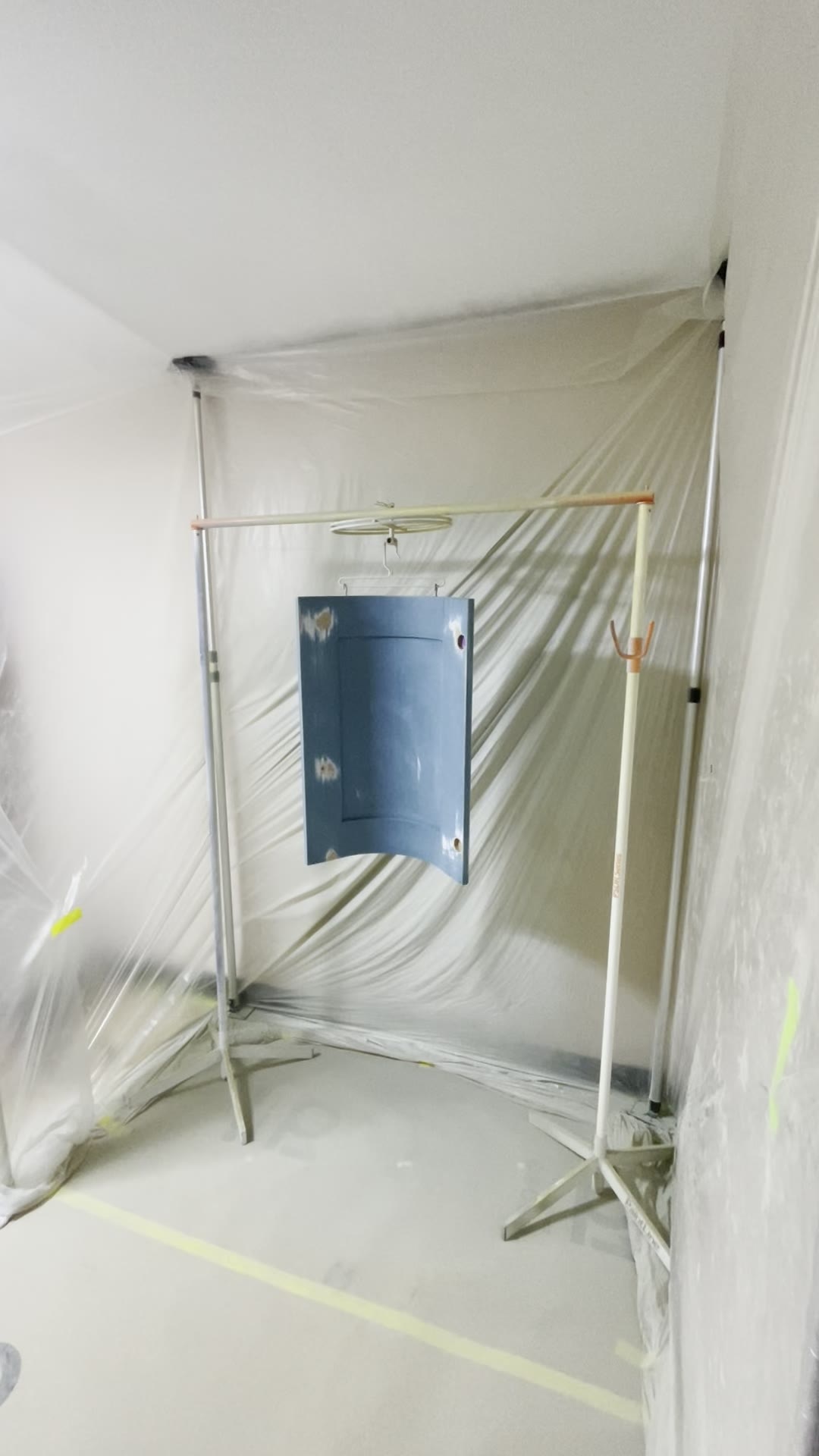 Kitchen cabinet door hanging on a spray rack inside a fully sheeted temporary spray booth in a London home