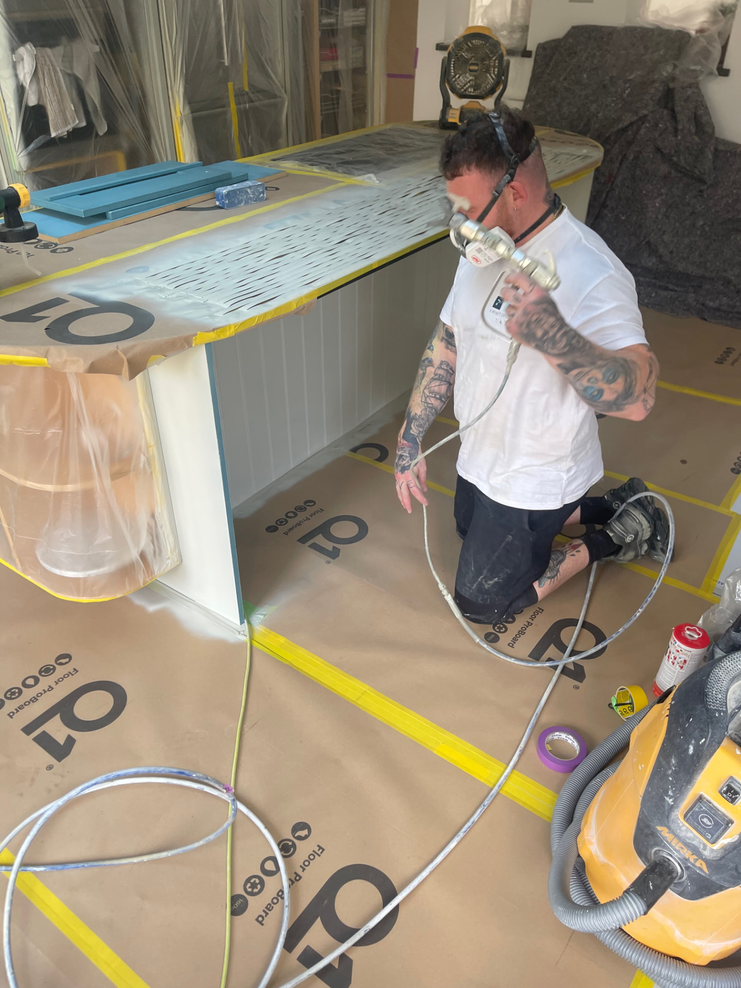 City & Guilds qualified sprayer applying Renner water-based coating to a kitchen island in a fully masked London kitchen
