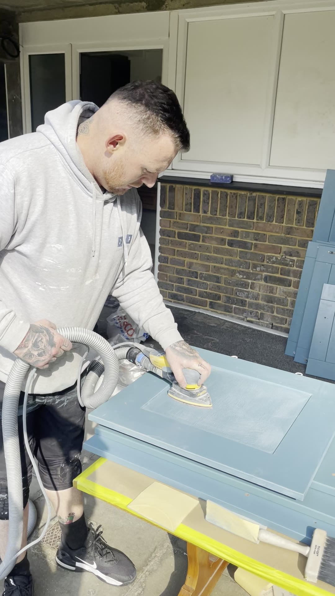 City & Guilds qualified sprayer sanding a blue kitchen cabinet door with a dust-extracted orbital sander
