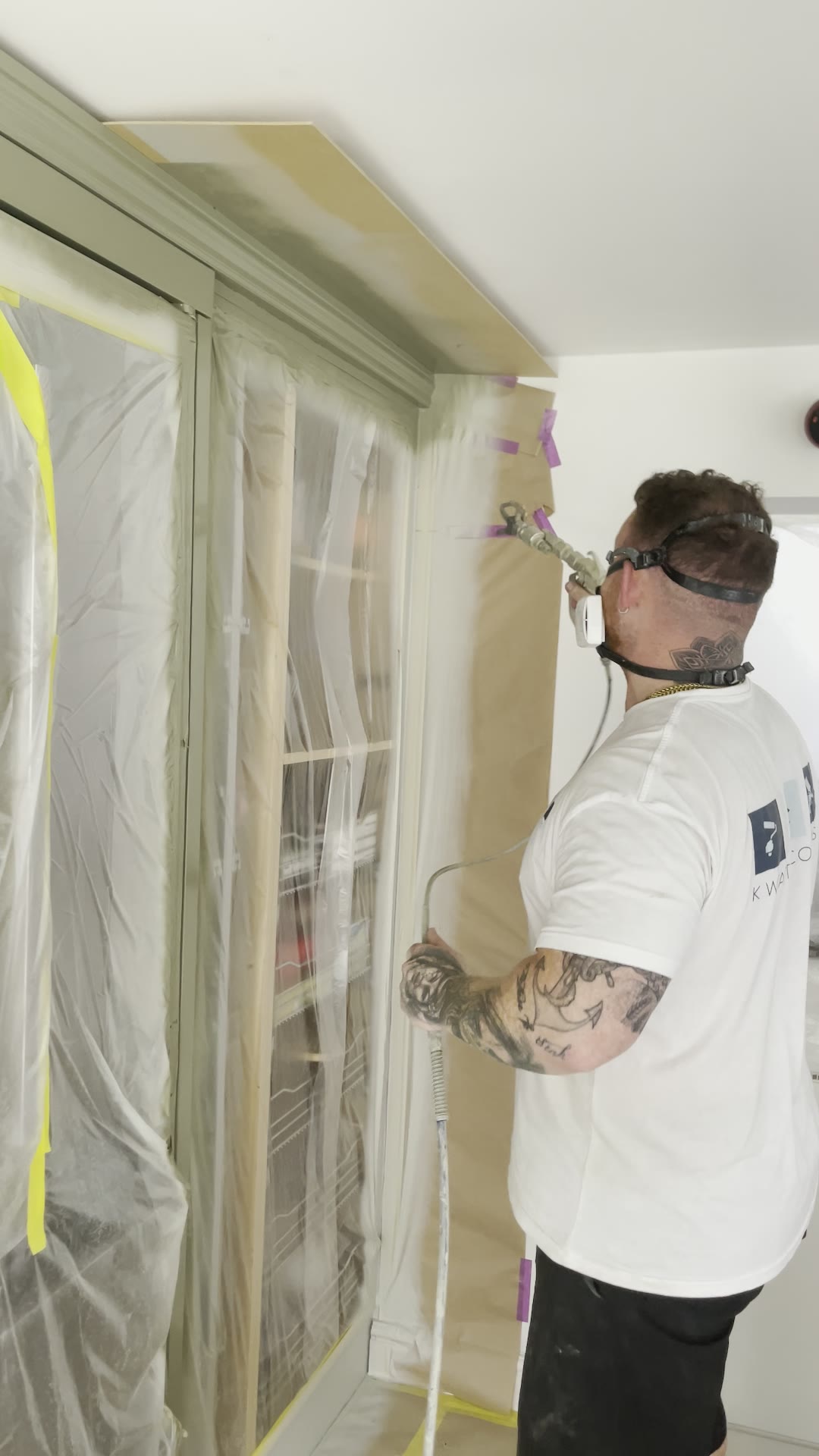 Professional decorator spraying a tall kitchen larder unit in sage green with a fine-finish spray gun
